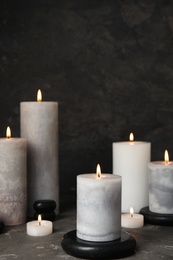 Photo of Burning candles and black spa stones on grey table, space for text