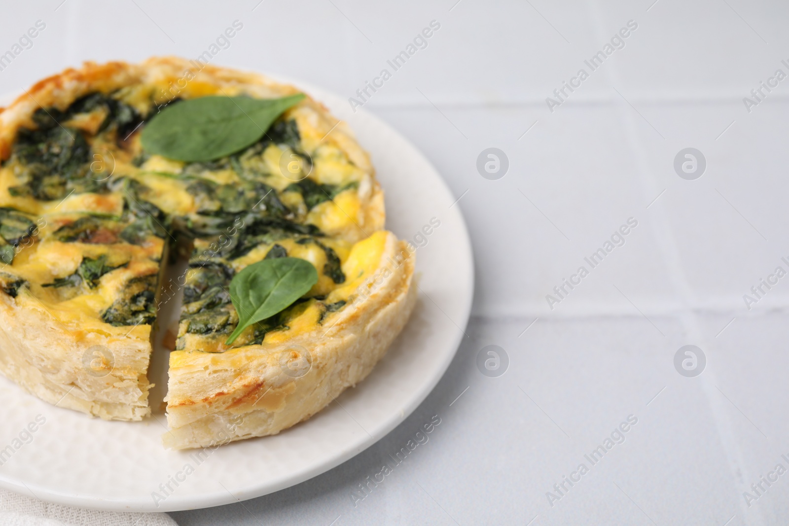 Photo of Delicious pie with spinach on white tiled table, closeup. Space for text