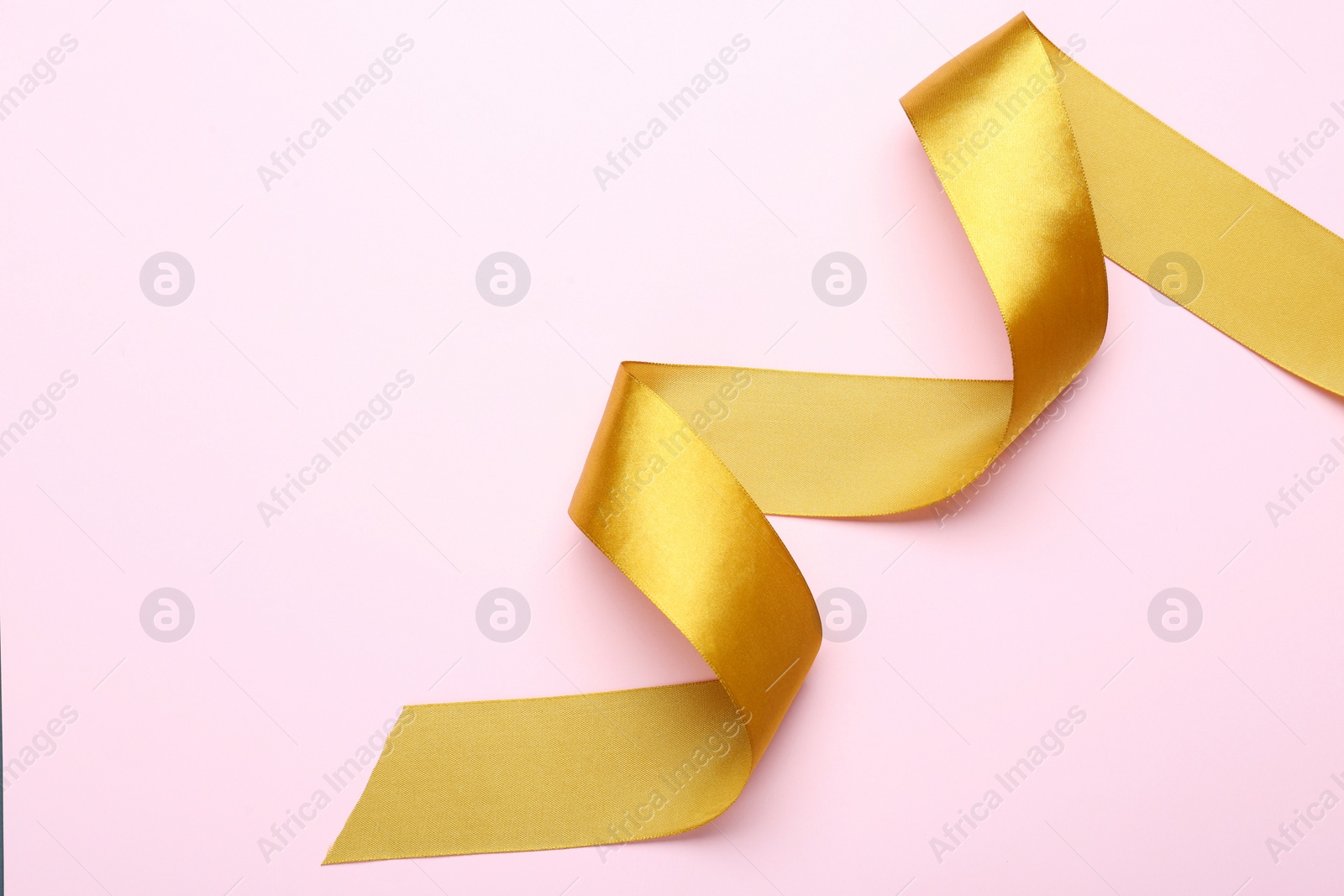 Photo of Beautiful golden ribbon on pink background, top view. Space for text