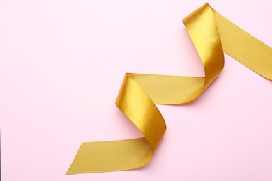 Photo of Beautiful golden ribbon on pink background, top view. Space for text