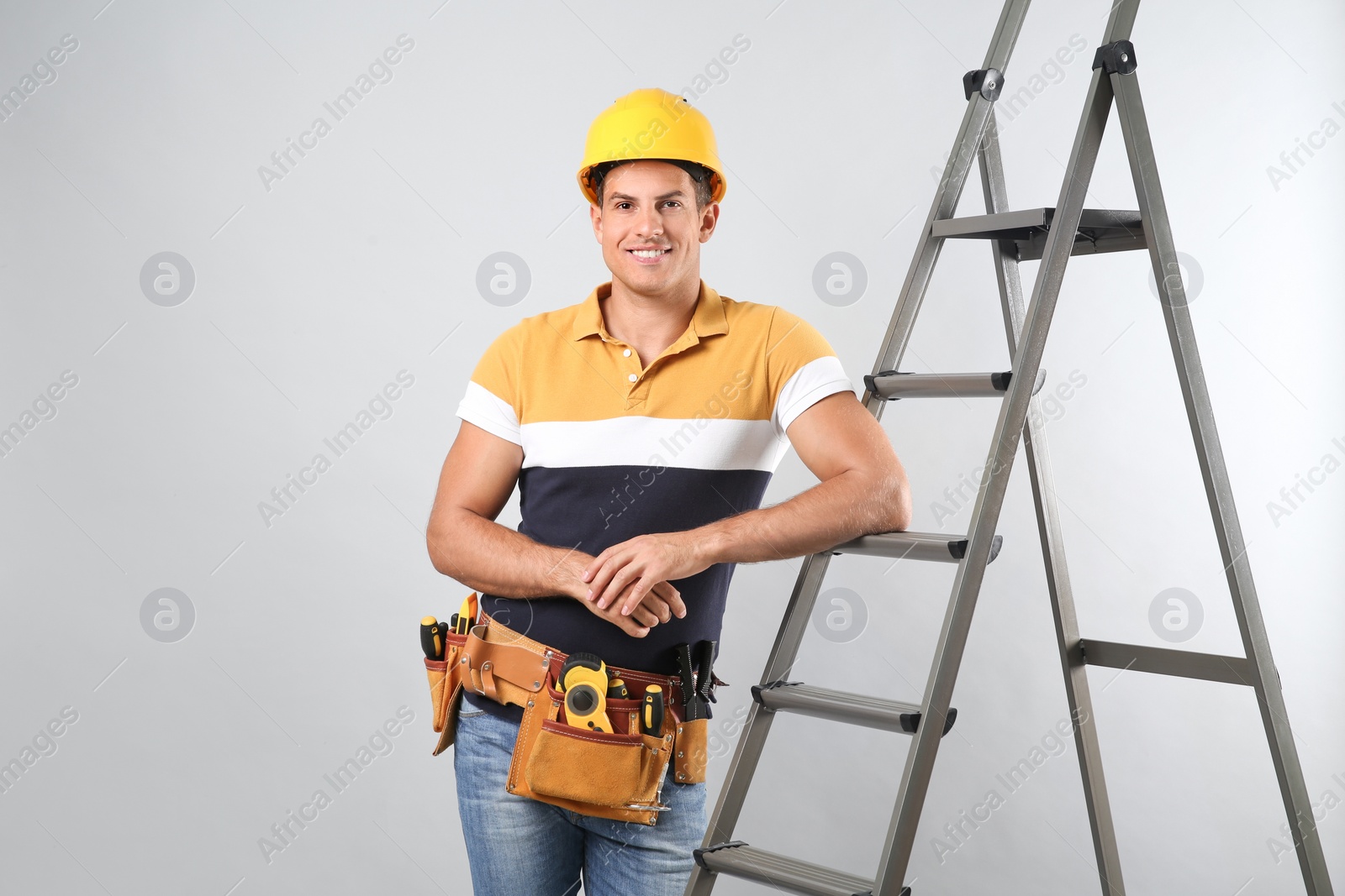 Photo of Professional builder near metal ladder on grey background