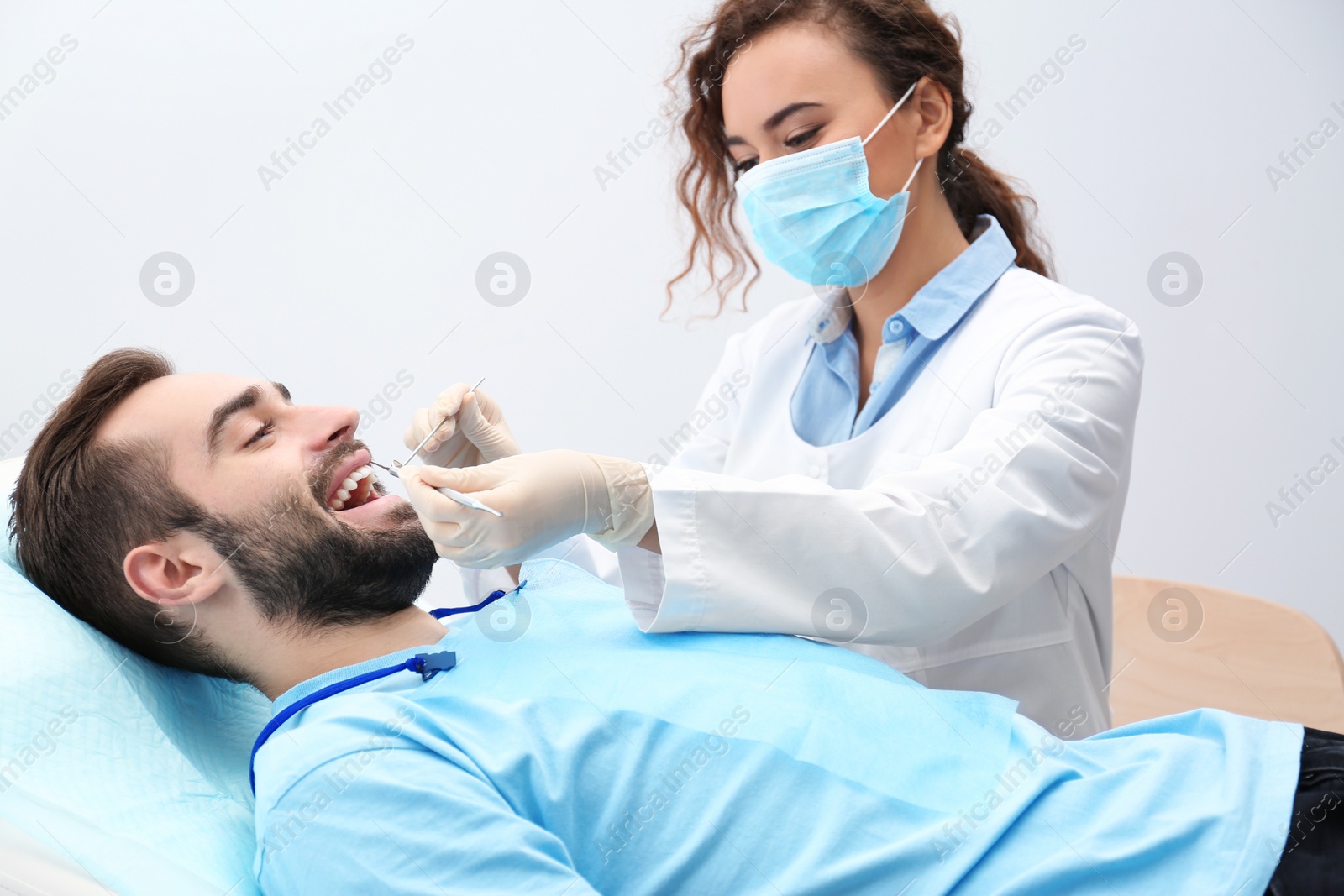 Photo of Dentist examining young man's teeth with mirror and probe in hospital