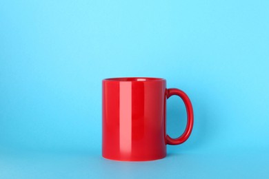 Photo of Blank red ceramic mug on light blue background