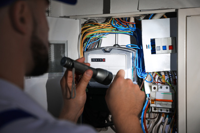 Photo of Electrician with flashlight fixing electric panel indoors