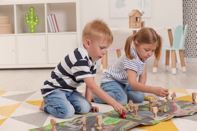 Photo of Little children playing with set of wooden road signs and toy cars indoors