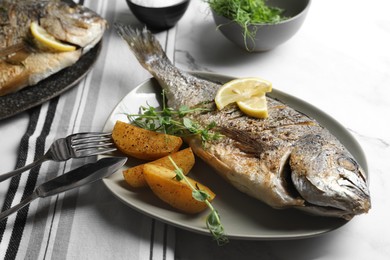 Photo of Seafood. Delicious baked fish served with lemon, potato and microgreens on light table, closeup