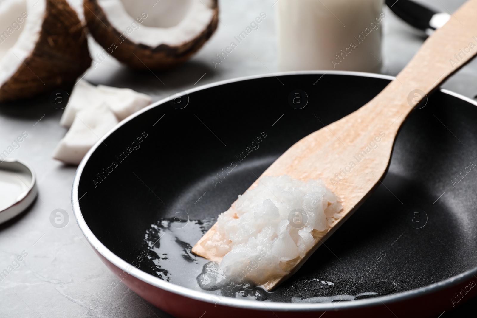 Photo of Frying pan with coconut oil and wooden spatula on table, closeup. Healthy cooking