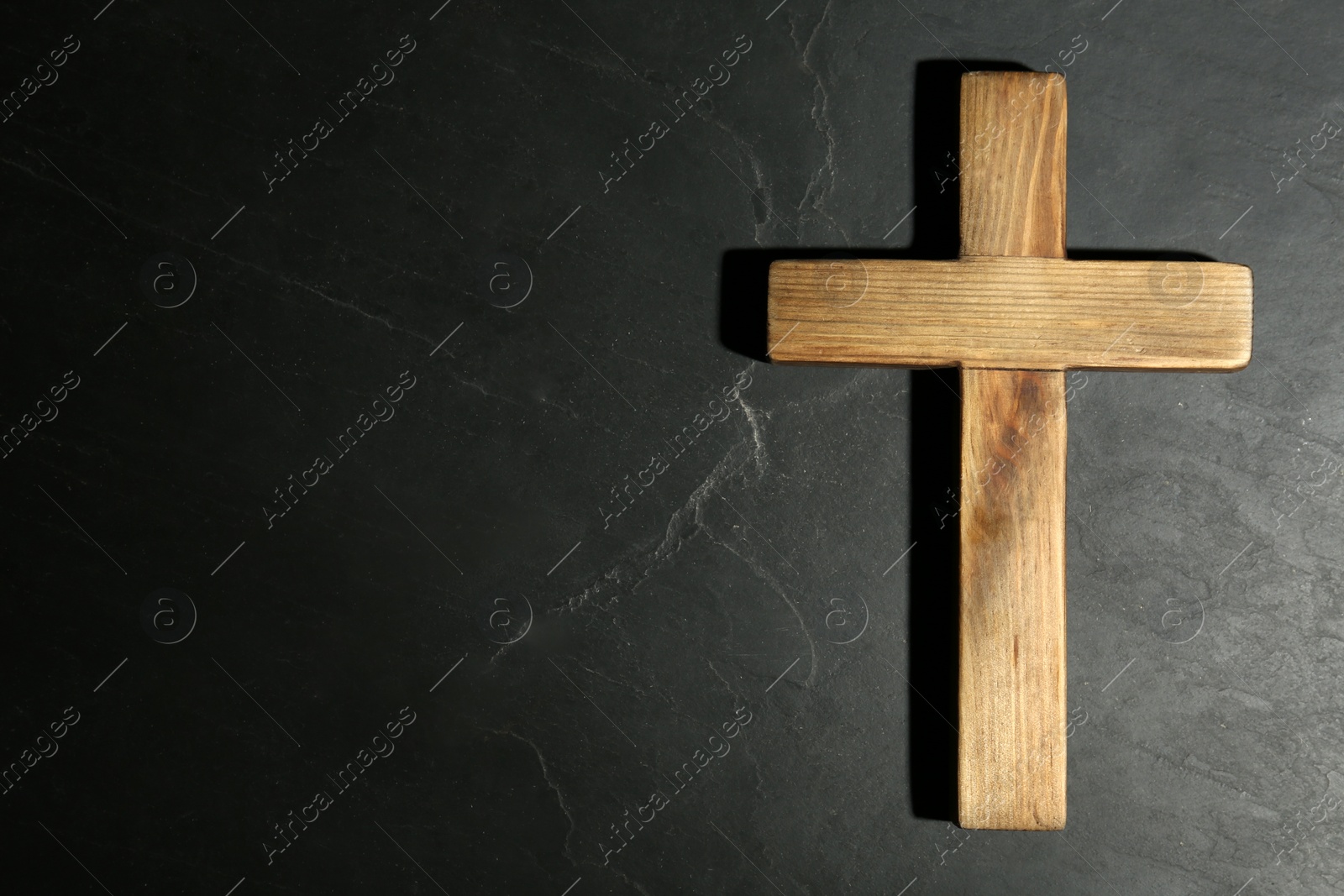 Photo of Wooden Christian cross on black slate table, top view with space for text. Religion concept