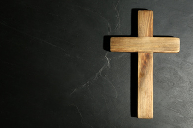 Photo of Wooden Christian cross on black slate table, top view with space for text. Religion concept