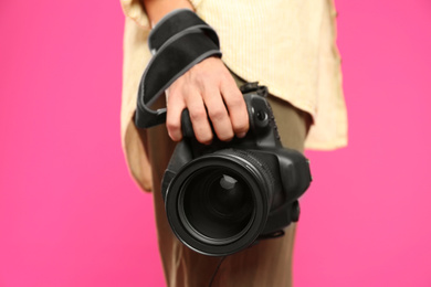 Photo of Professional photographer with modern camera on pink background in studio, closeup