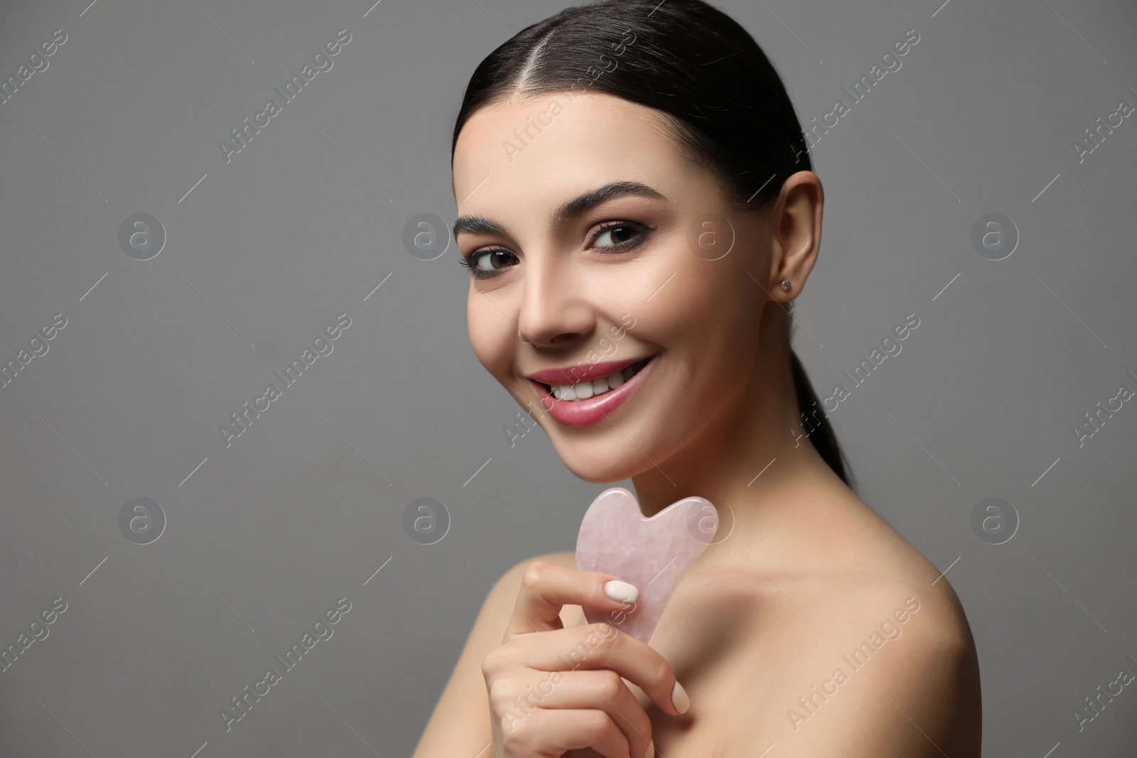 Photo of Beautiful young woman doing facial massage with gua sha tool on grey background. Space for text