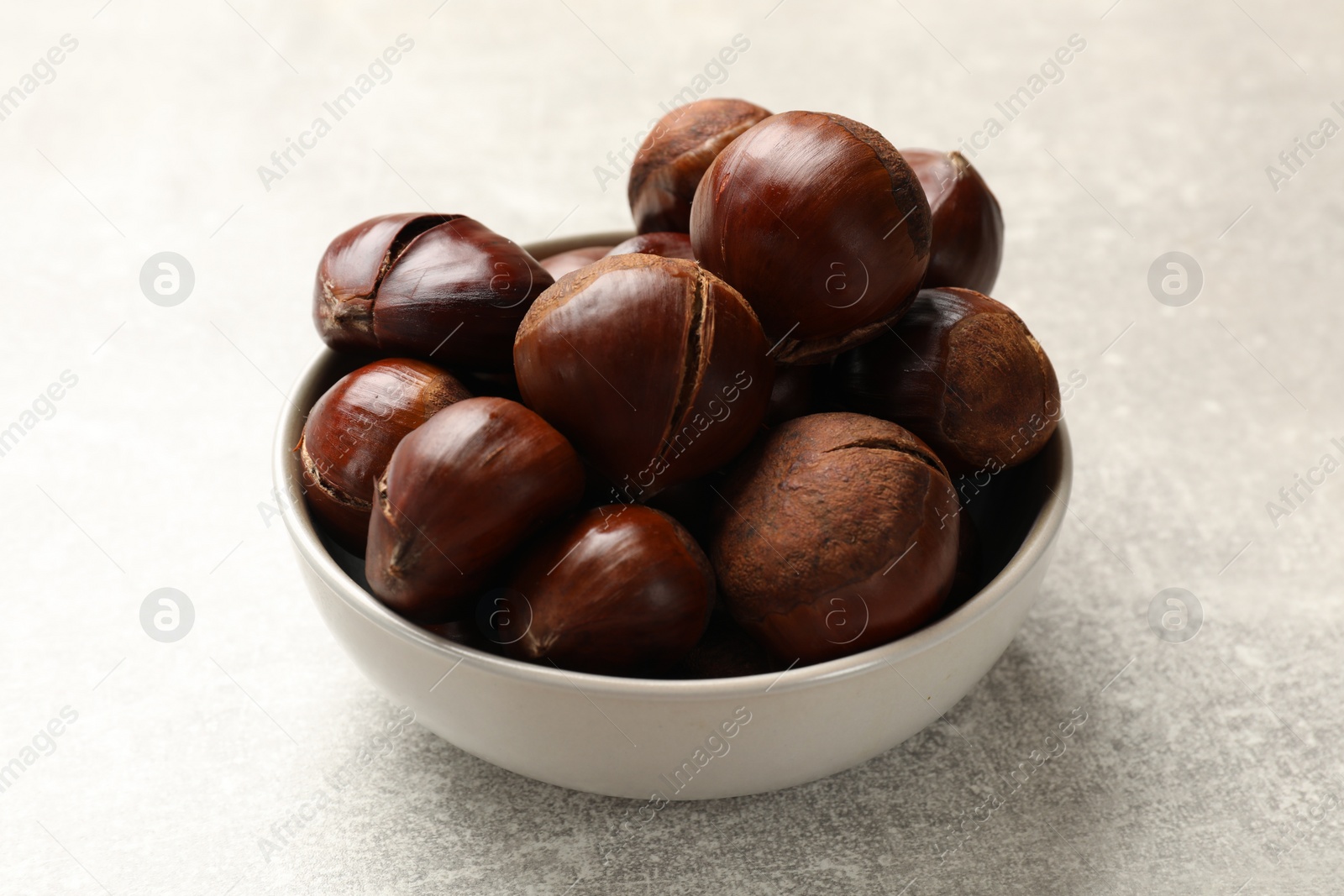 Photo of Fresh edible sweet chestnuts in bowl on grey table