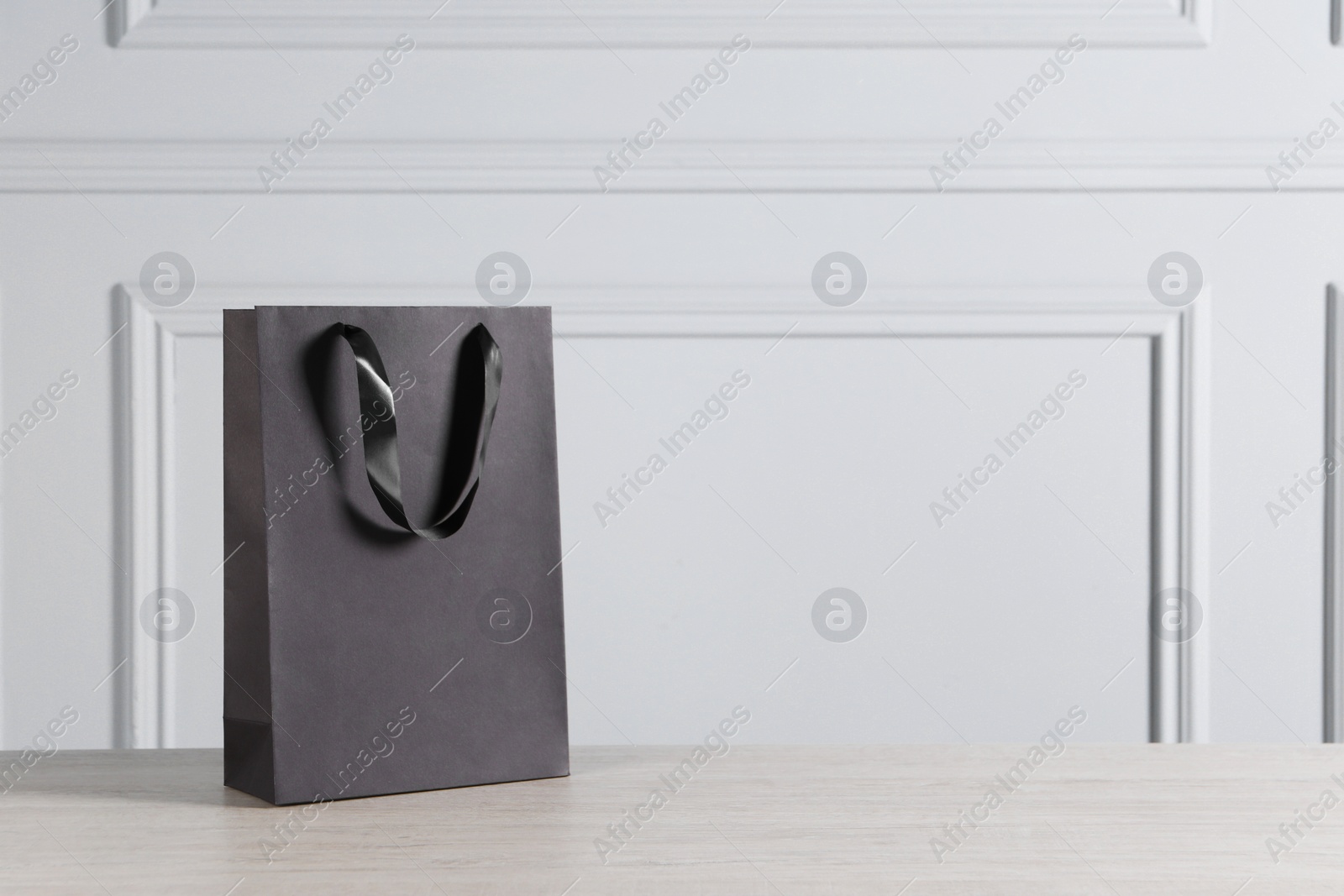 Photo of Black paper bag on wooden table against light grey wall, space for text