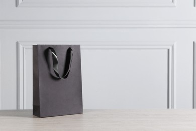 Black paper bag on wooden table against light grey wall, space for text