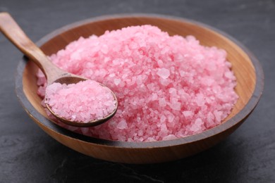 Photo of Bowl and spoon with pink sea salt on black table, closeup