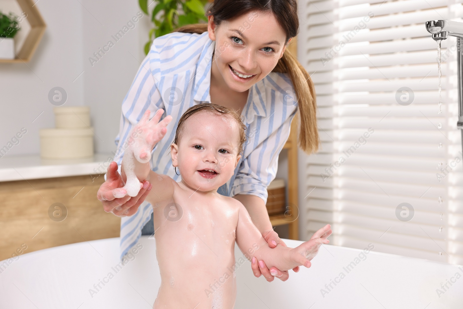 Photo of Mother bathing her cute little baby in tub at home