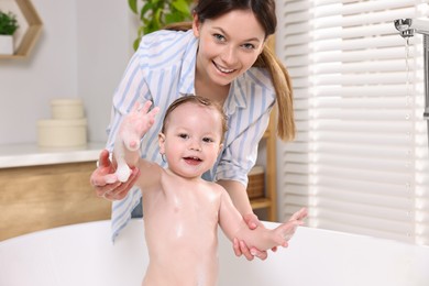 Mother bathing her cute little baby in tub at home