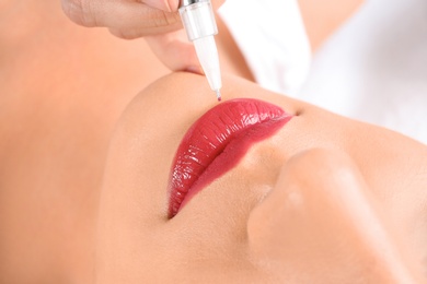 Photo of Young woman getting permanent makeup on lips in beautician salon, closeup