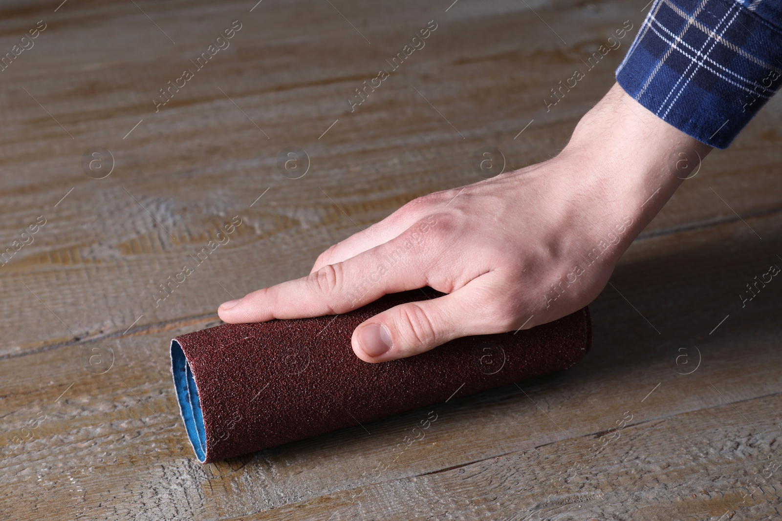 Photo of Man polishing wooden table with rolled sheet of sandpaper, closeup