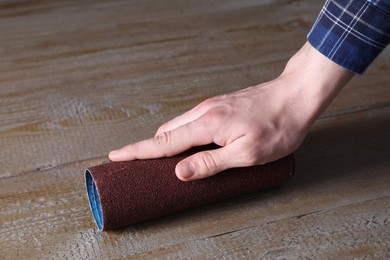 Man polishing wooden table with rolled sheet of sandpaper, closeup
