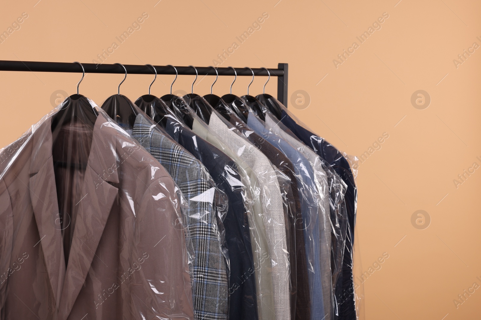 Photo of Dry-cleaning service. Many different clothes in plastic bags hanging on rack against beige background, space for text