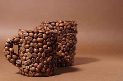 Cups made of coffee beans on brown background. Space for text