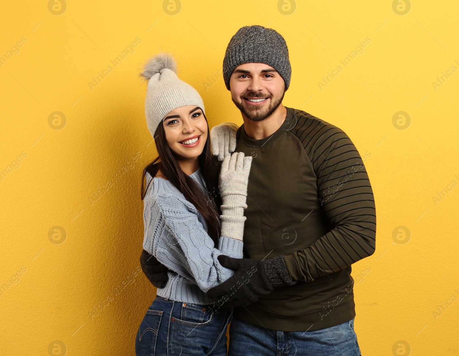 Photo of Happy young couple in warm clothes on yellow background. Winter vacation