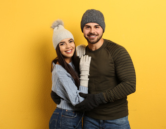 Photo of Happy young couple in warm clothes on yellow background. Winter vacation