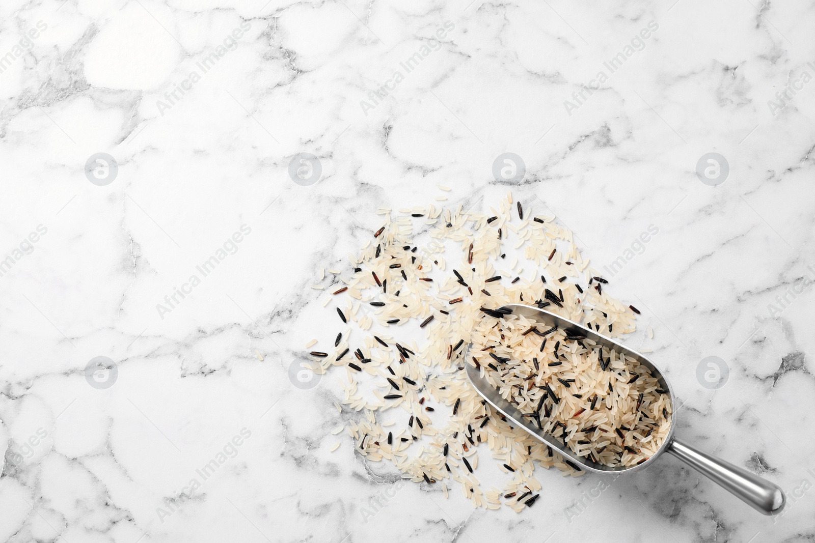 Photo of Mix of brown and polished rice with scoop on marble table, top view. Space for text