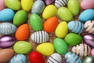 Photo of Many painted Easter eggs on burlap, flat lay