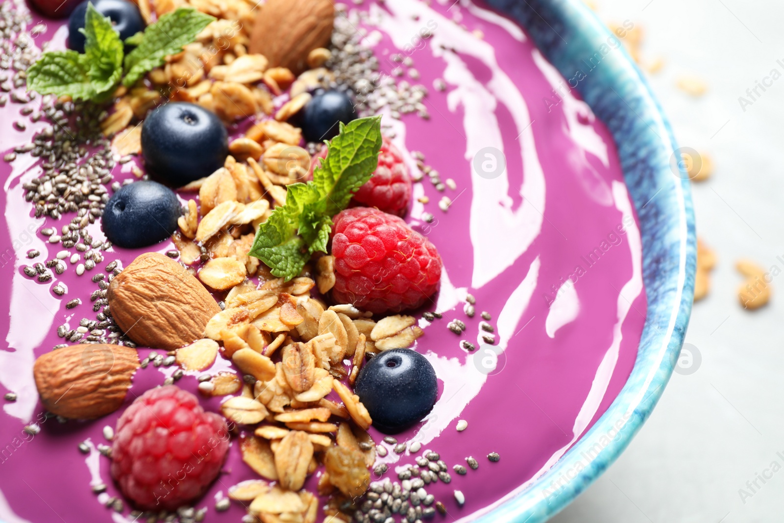 Photo of Delicious acai smoothie with granola and berries in dessert bowl on table, closeup