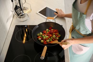 Photo of Young woman with tablet cooking on stove in kitchen, closeup