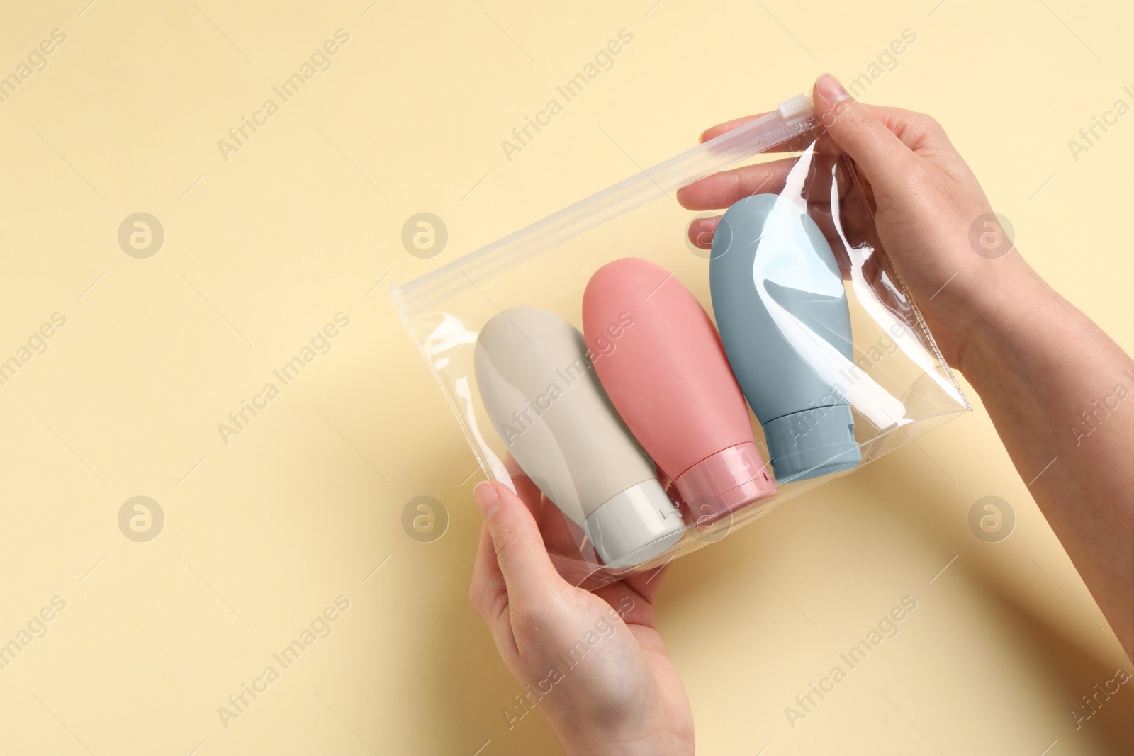 Photo of Cosmetic travel kit. Woman holding plastic bag with small bottles of personal care products against beige background, closeup. Space for text