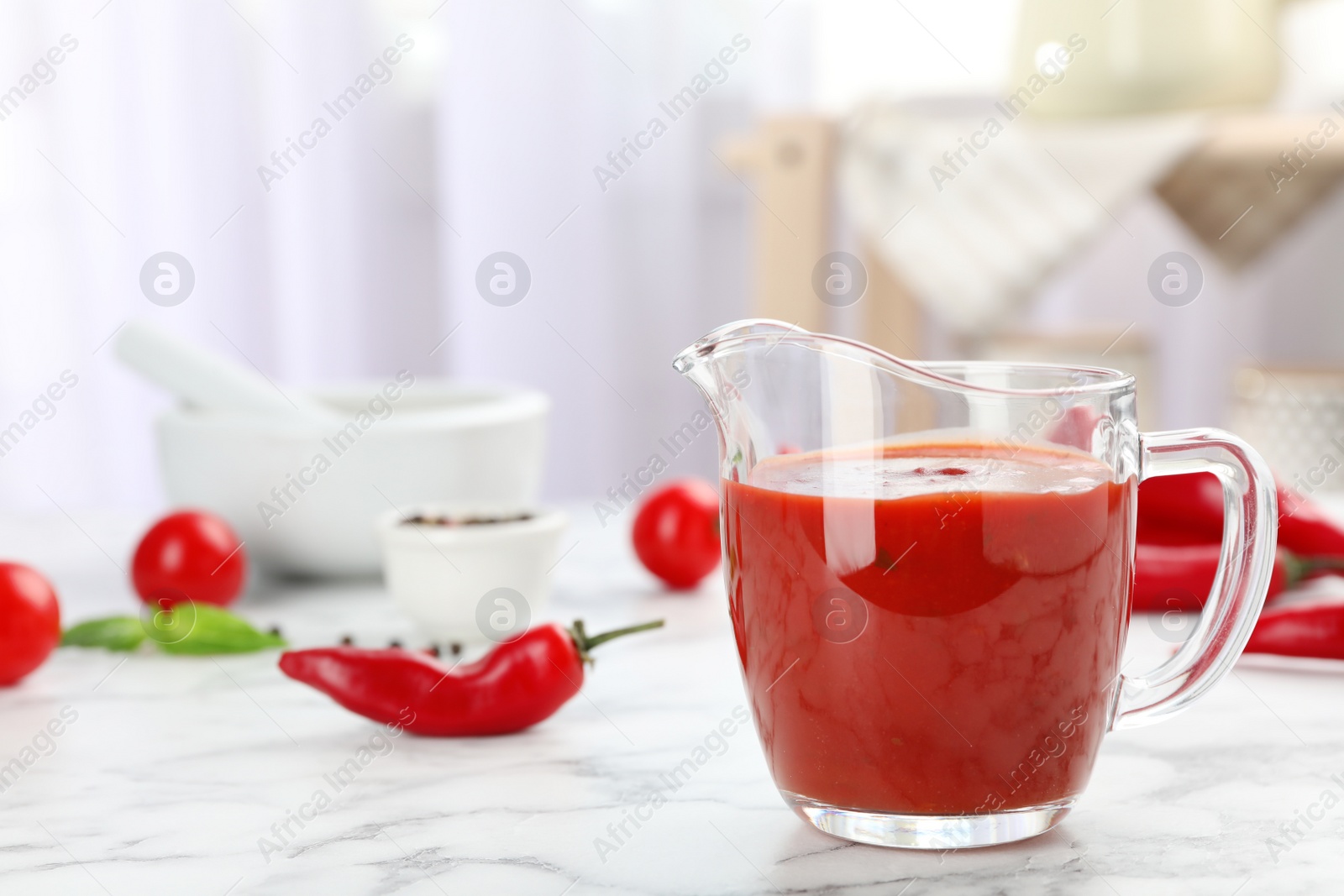 Photo of Jug with spicy chili sauce on marble table