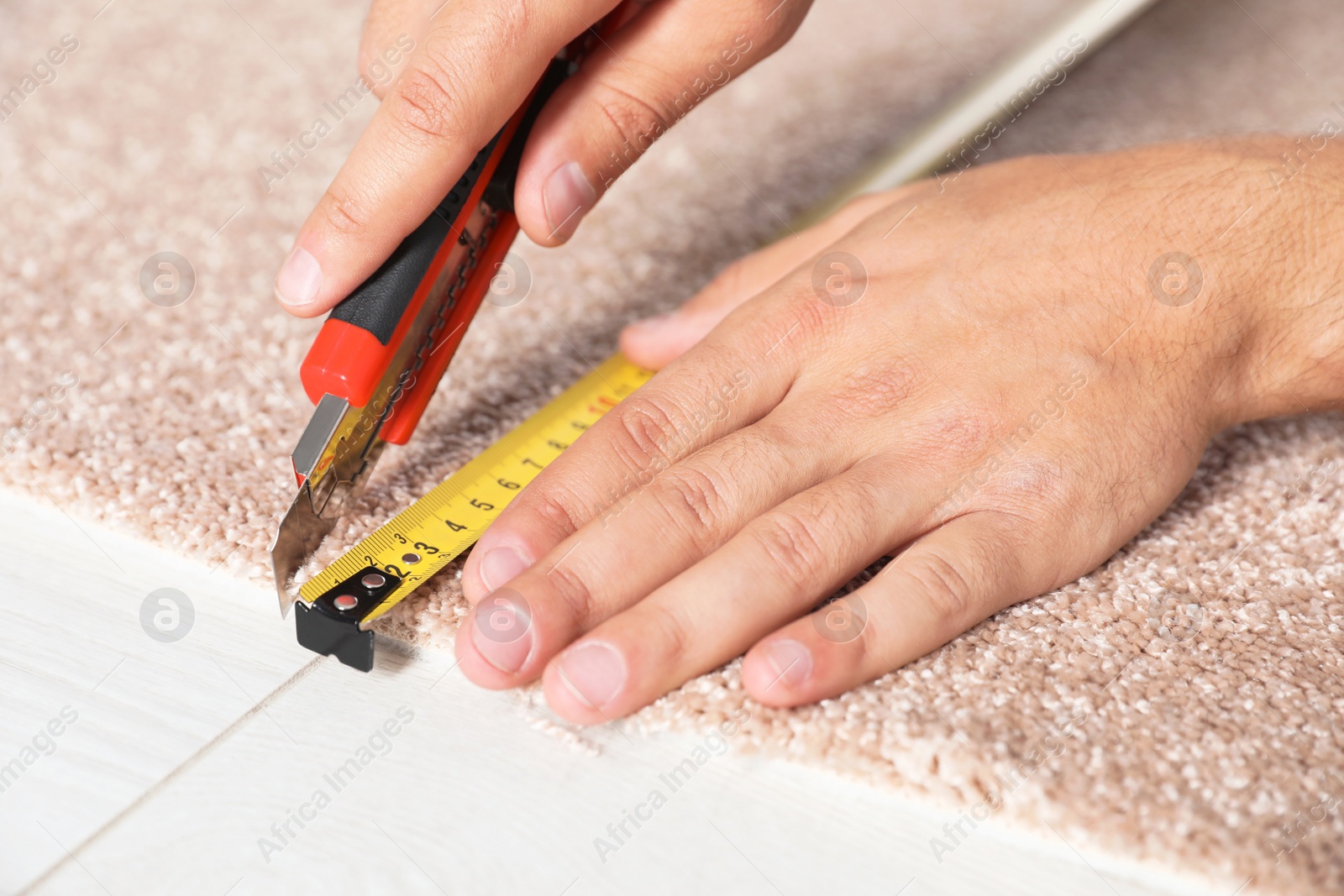 Photo of Man cutting new carpet flooring indoors, closeup