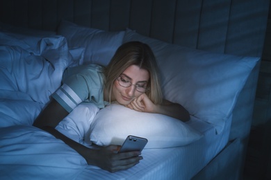 Photo of Young woman using smartphone in bed at night. Nomophobia and sleeping disorder problem