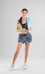 Beautiful young woman in sportswear with towel and bottle of water on white background