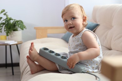 Photo of Cute baby playing with power strip on sofa at home. Dangerous situation