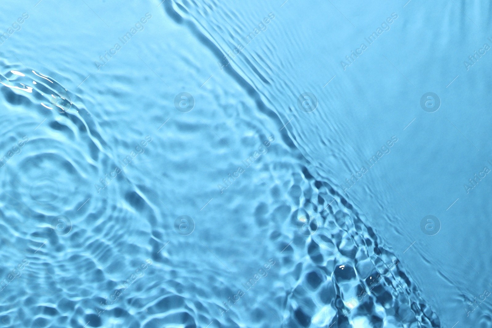 Image of Rippled surface of clear water on light blue background, closeup