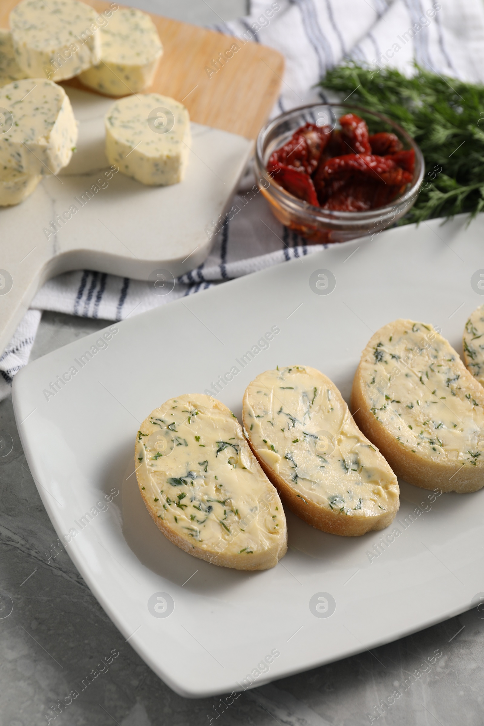 Photo of Tasty butter, dill, chili peppers and bread on grey marble table