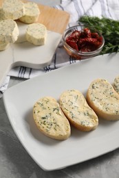 Photo of Tasty butter, dill, chili peppers and bread on grey marble table