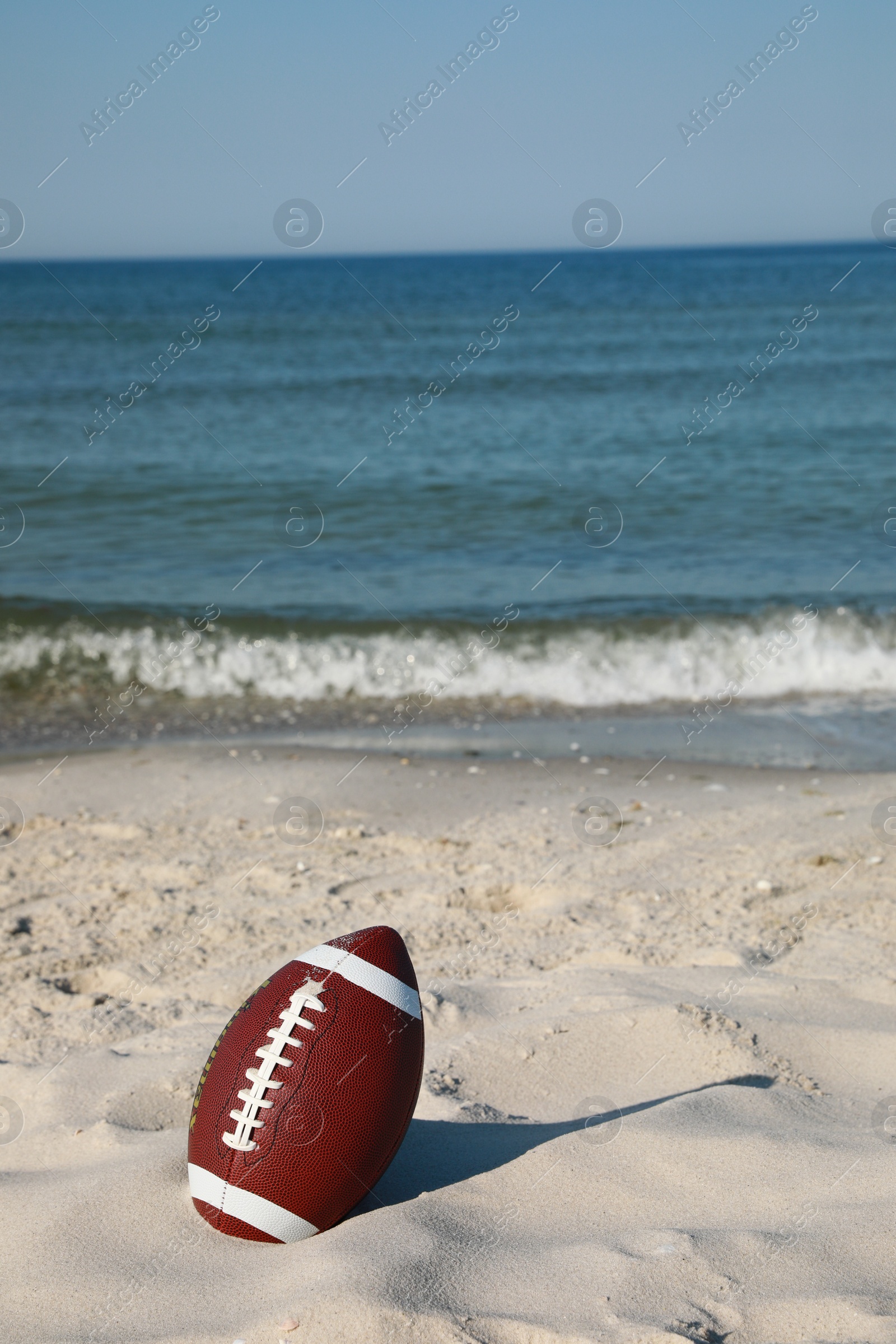Photo of American football ball on beach. Space for text