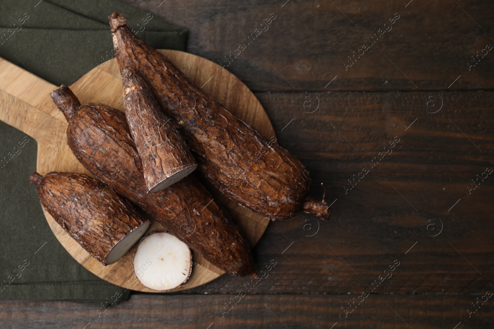 Photo of Whole and cut cassava roots on wooden table, top view. Space for text