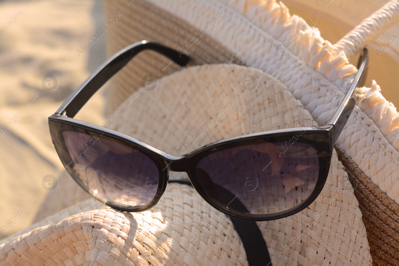 Photo of Hat and bag with beautiful sunglasses on sandy beach, closeup