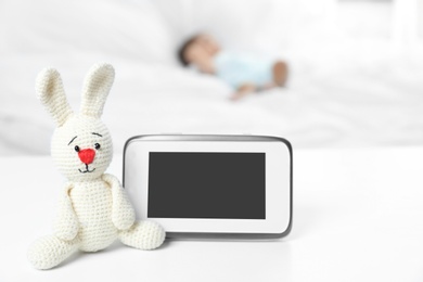 Photo of Baby monitor and toy on table near bed with child in room. Video nanny