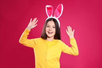 Photo of Portrait of little girl in Easter bunny ears headband on color background
