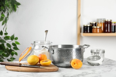 Pot with apricots and sugar on white marble table indoors. Making delicious jam