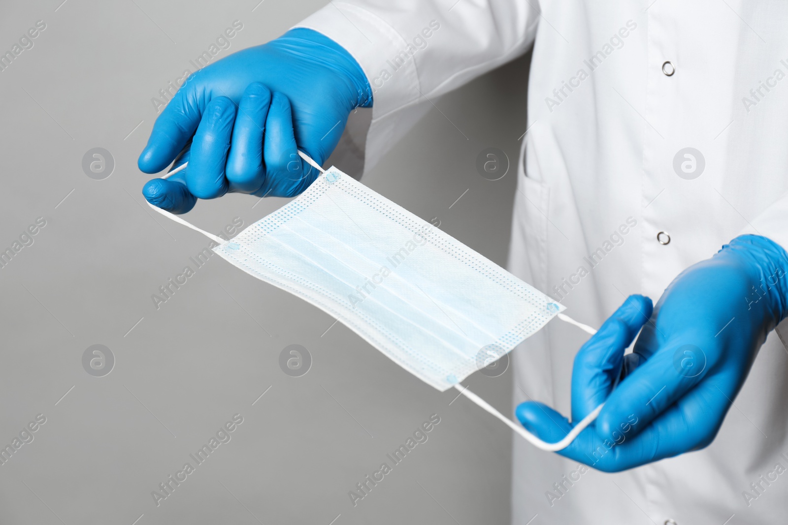 Photo of Doctor in medical gloves holding protective mask on light grey background, closeup