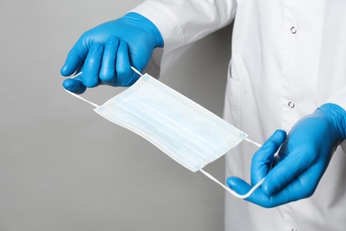Photo of Doctor in medical gloves holding protective mask on light grey background, closeup