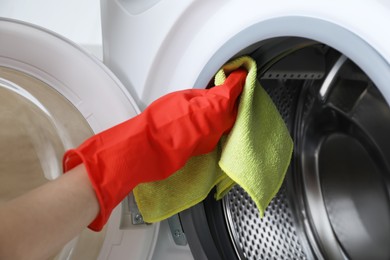 Photo of Woman cleaning washing machine with rag, closeup